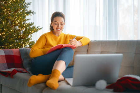 Woman is making notes sitting on the sofa in the living room decorated for Christmas.の写真素材