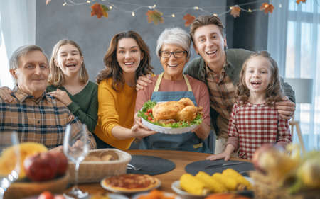Thanksgiving Day, Autumn feast. Happy family sitting at the table and celebrating holiday. Grandparents, mother, father and children. Traditional dinner.の写真素材