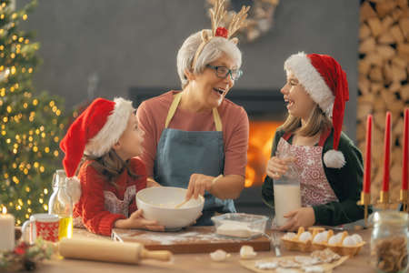 Merry Christmas and Happy Holidays. Family preparation holiday food. Grandma and granddaughters cooking cookies.の写真素材