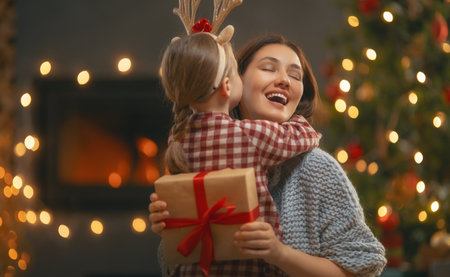 Merry Christmas and Happy Holidays. Cheerful mother and her cute daughter girl exchanging gifts. Mom and little child having fun near tree indoors. Loving family with presents in room.の写真素材