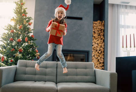 Merry Christmas and Happy Holidays! Cheerful cute child girl with gift. Kid is having fun near tree.の写真素材