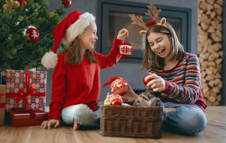 Merry Christmas and Happy Holidays. Cheerful cute childrens girls at home. Kids are having fun near tree in the morningの写真素材