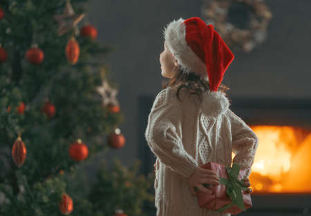 Merry Christmas and Happy Holidays! Cheerful cute child girl with gift. Kid is having fun near tree.の写真素材
