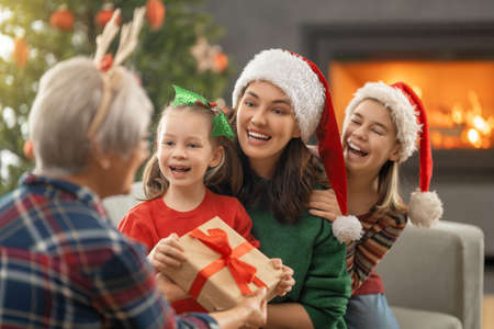 Merry Christmas and Happy Holidays. Cheerful kids presenting gifts to mom and granny. Parents and...
