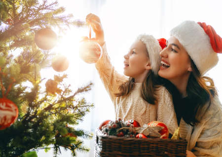 Merry Christmas and Happy Holidays. Mom and daughter near the tree indoors. The morning before Xmas. Portrait loving family close up.の写真素材