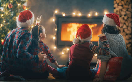 Merry Christmas and Happy Holidays. Mom, dad and their cute daughters looking at fireplace. Parents and children having fun near tree indoors.の写真素材