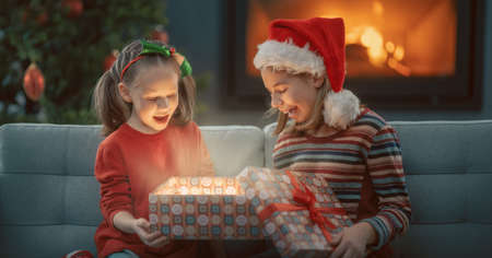 Merry Christmas and Happy Holidays! Cheerful cute childrens girls opening gifts. Kids are having fun near tree in the evening. Loving family with presents in room.の写真素材