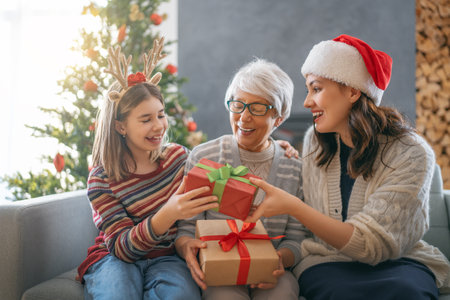 Merry Christmas and Happy Holidays. Cheerful kid presenting gifts to mom and granny. Parents and little child having fun near tree indoors. Loving family with presents in room.の写真素材