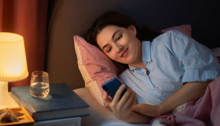 Happy casual beautiful woman is using a phone in the bed at home.