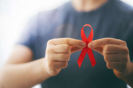 World Aids Day. Red ribbon in the hands close up