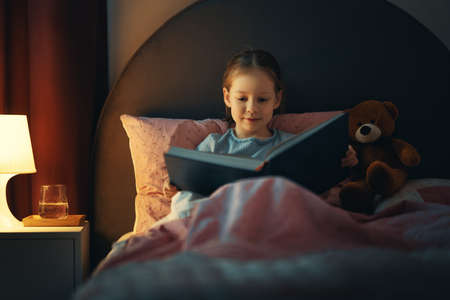 Cute little girl is reading a book in her bedroom.の写真素材