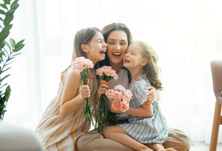 Happy day! Children daughters are congratulating mother and giving her flowers. Mum and girls smiling and hugging. Family holiday and togetherness.の写真素材
