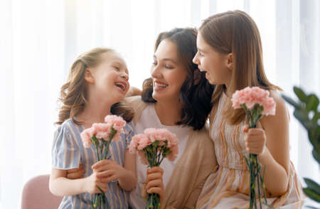 Happy day! Children daughters are congratulating mother and giving her flowers. Mum and girls smiling and hugging. Family holiday and togetherness.の写真素材
