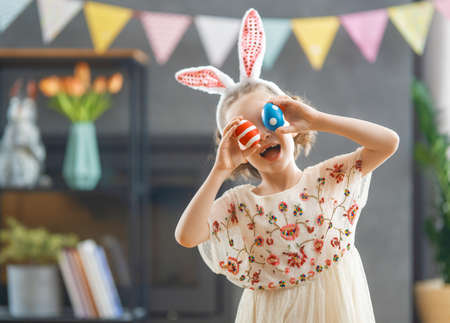 Beautiful child with painting eggs. Happy family preparing for Easter. Cute little girl is wearing bunny ears.の写真素材