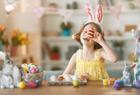 Beautiful child painting eggs. Happy family preparing for Easter. Cute little girl is wearing bunny ears.の写真素材