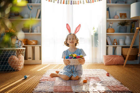 Beautiful child with painting eggs. Happy family preparing for Easter. Cute little girl is wearing bunny ears.の写真素材