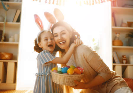 Happy holiday! Mother and her daughter with painting eggs. Family celebrating Easter. Cute little...