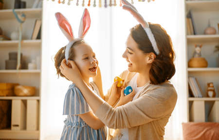 Happy holiday! Mother and her daughter with painting eggs. Family celebrating Easter. Cute little...