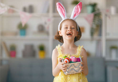 Beautiful child with painting eggs. Happy family preparing for Easter. Cute little girl is wearing bunny ears.の写真素材