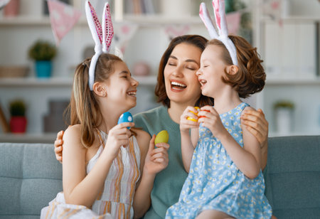 Happy holiday! Mother and her daughters with painting eggs. Family celebrating Easter. Cute little...