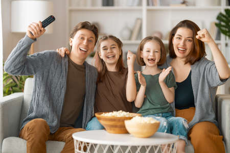 Happy family watching projector, TV, movies with popcorn in the evening at home. Mother, father and daughters spending time together.の写真素材