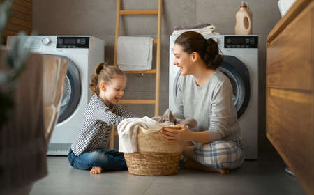 Beautiful young woman and child girl little helper are having fun and smiling while doing laundry at home.の写真素材