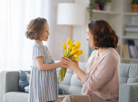 Happy mother's day. Child daughter congratulating mom and giving her flowers. Mum and girl smiling and hugging. Family holiday and togetherness.の写真素材