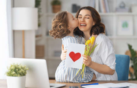 Happy mother's day. Child daughter congratulating mom and giving her flowers and card. Mum and girl smiling and hugging. Family holiday and togetherness.の写真素材