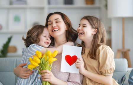 Happy mother's day. Children daughters are congratulating mom and giving her flowers. Mum and girls smiling and hugging. Family holiday and togetherness.の写真素材