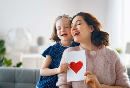 Happy mother's day. Child daughter is congratulating mom and giving her postcard. Mum and girl smiling and hugging. Family holiday and togetherness.の写真素材