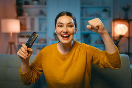 Young woman watching projector, TV, movies in the evening. Girl spending time at home.