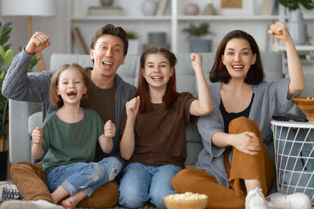 Happy family watching projector, TV, movies with popcorn in the evening at home. Mother, father and daughters spending time together.の写真素材