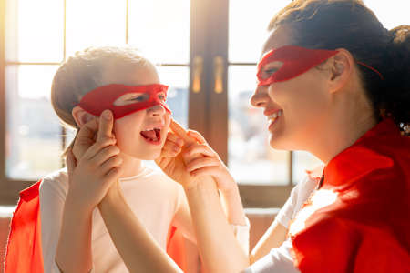 Mother and her child playing together. Girl and mom in Superhero costume. Mum and kid having fun. Family holiday and togetherness.の写真素材