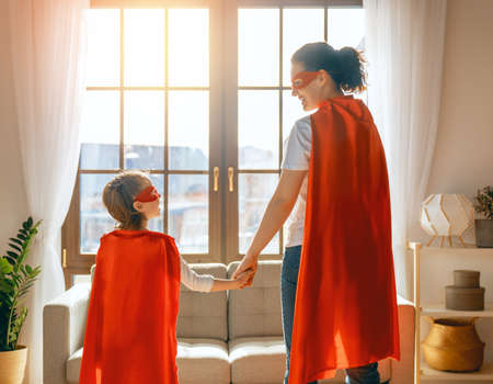 Mother and her child playing together. Girl and mom in Superhero costume. Mum and kid having fun. Family holiday and togetherness.の写真素材