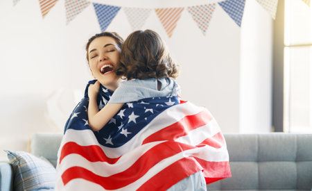 Patriotic holiday. Happy family, mom and daughter child girl with American flag at home. The USA celebrate 4th of July.の写真素材