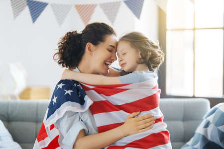 Patriotic holiday. Happy family, mom and daughter child girl with American flag at home. The USA celebrate 4th of July.の写真素材