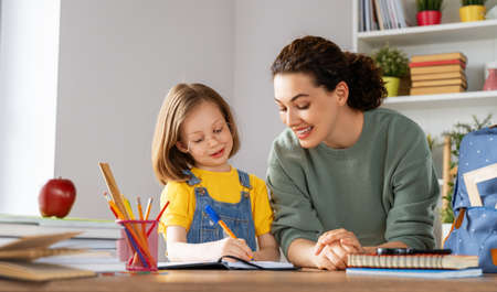 Happy child and adult are sitting at desk. Girl doing homework or education.の写真素材