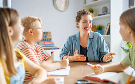 Happy kids and teacher at school. Woman and children are talking in the class.