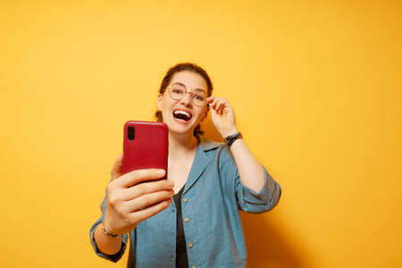 Happy young woman with smartphone on background of yellow wall.