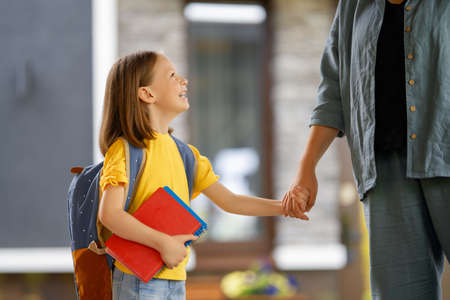 Parent and pupil of primary school going hand in hand. Woman and girl with backpack behind the back. Beginning of lessons.の写真素材