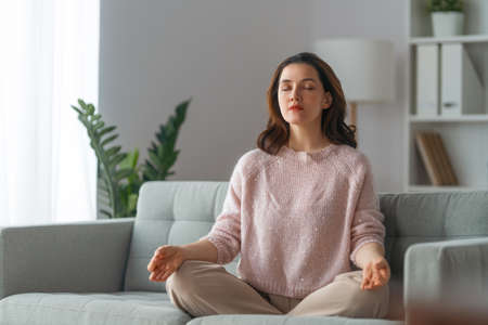 Happy young woman enjoying sunny morning and practicing meditation on the sofa at home.の写真素材