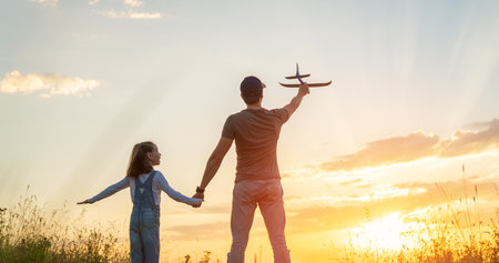 Happy family, father and kid with toy plane are playing on the field at sunset.の写真素材