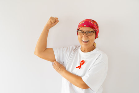 Smiling senior woman with red satin ribbon symbolizing concept of illness awareness, expressing solidarity and support for cancer patients and survivors.の写真素材