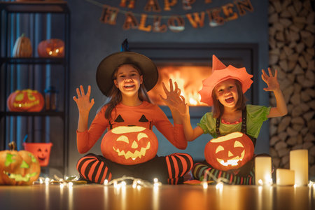 Happy sisters on Halloween. Funny kids in carnival costumes indoors. Cheerful children play with pumpkins and candy near fireplace at home.の写真素材