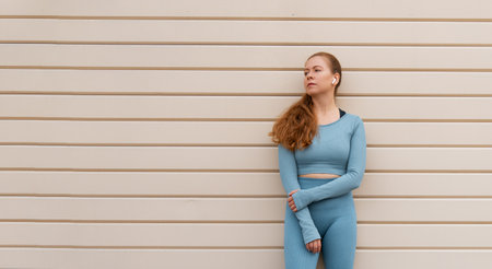 Sportive woman is standing against the wall. Girl is listening music in a urban area. Concept of...