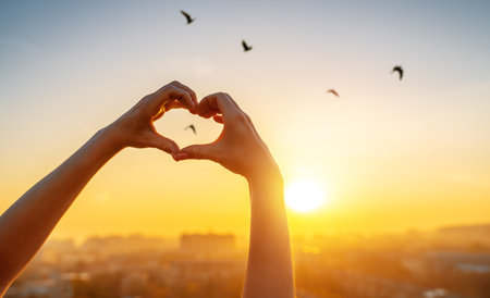 Female hands in the form of heart against the sunset sky.の写真素材