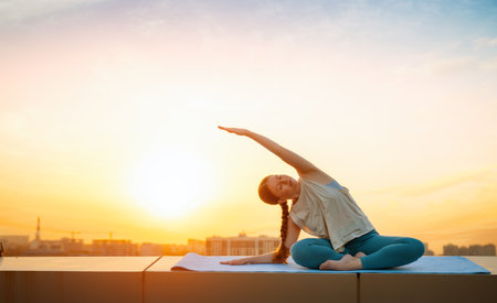 Young sportswoman is doing yoga exercise on rooftop of parking, garage in summer day morning.の写真素材