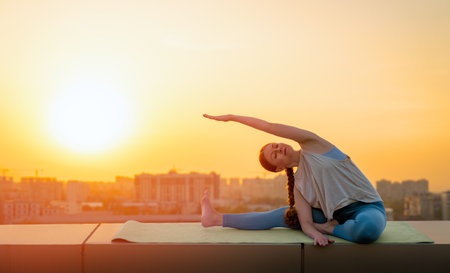 Young sportswoman is doing yoga exercise on rooftop of parking, garage in summer day morning.の写真素材