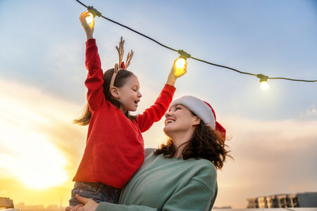Merry Christmas and Happy Holidays! Happy mother and daughter are decorating home terrace or balcony with garlands.の写真素材