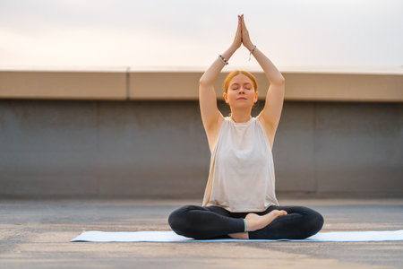 Young sportswoman is doing yoga exercise on rooftop of parking, garage in summer day morning.の写真素材